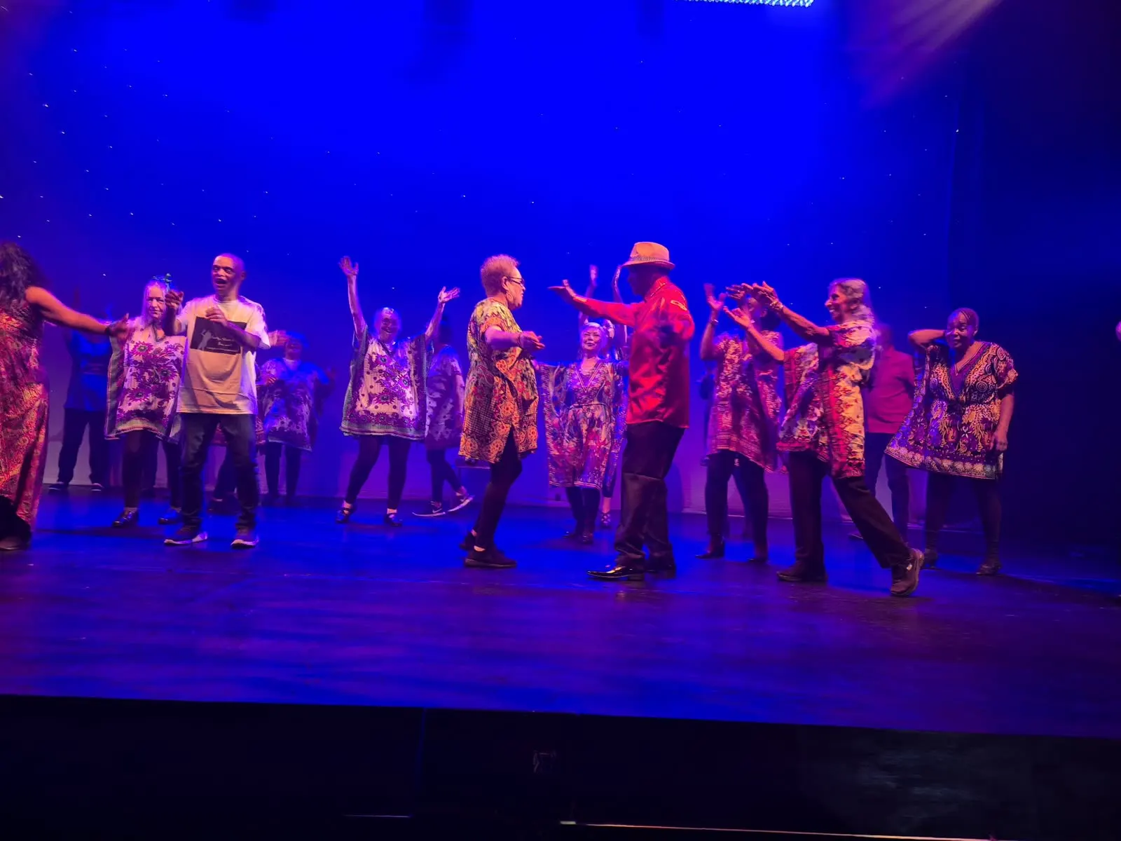 BADGE dancers in patterned costumes on stage under blue lights, arms raised