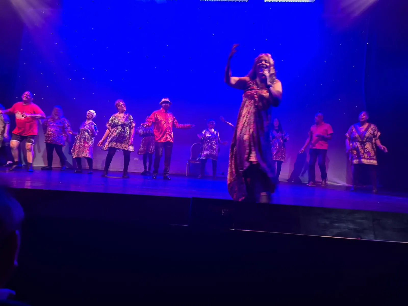 A singer performs at the front of the stage while BADGE dancers move behind her